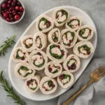 Turkey Cranberry Pinwheels arranged on a white platter with cranberries and rosemary