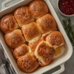 Baked Turkey Cranberry Sliders with brie and poppy seed butter tops in a baking dish