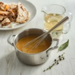 Turkey Gravy from Stock in a saucepan with a whisk beside a pitcher of stock